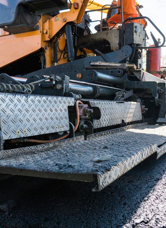 Worker operating asphalt paver machine during road construction and repairing works. A paver finisher, asphalt finisher or paving machine placing a layer of asphalt. Repaving